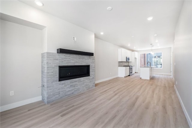 unfurnished living room featuring recessed lighting, light wood-style flooring, baseboards, and a stone fireplace