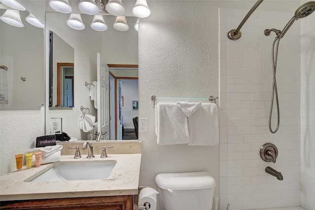 bathroom with a textured wall, walk in shower, vanity, and toilet