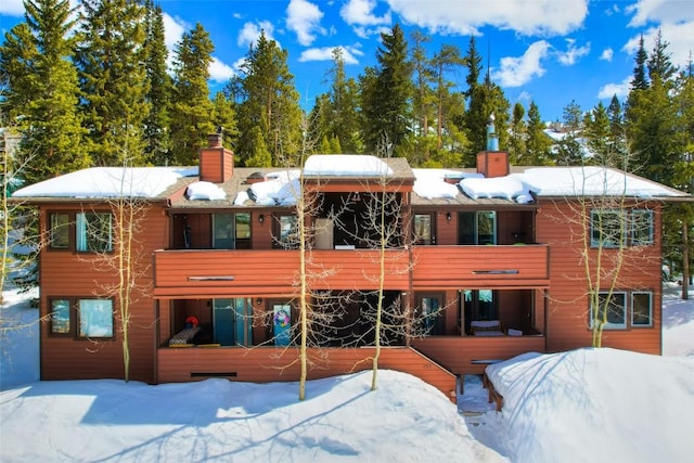 snow covered back of property featuring a chimney