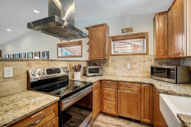 kitchen featuring light wood-style flooring, a toaster, island range hood, brown cabinetry, and appliances with stainless steel finishes