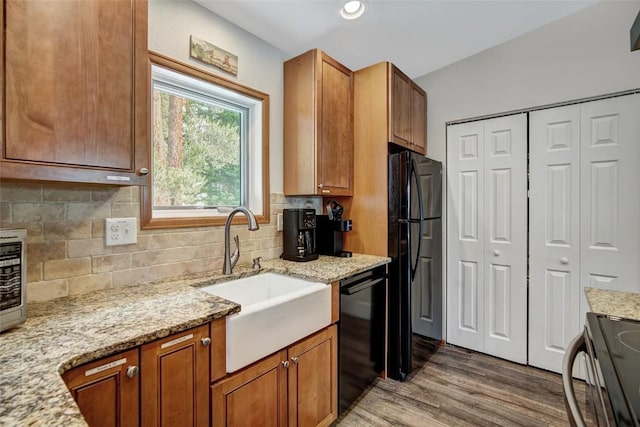 kitchen with a sink, brown cabinets, black appliances, and tasteful backsplash