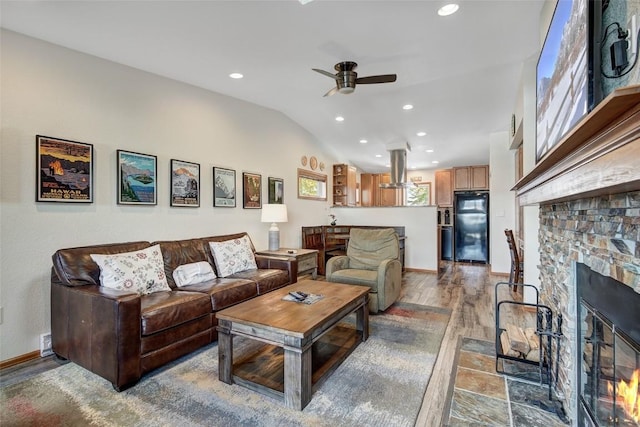 living room featuring recessed lighting, light wood-type flooring, a ceiling fan, a stone fireplace, and lofted ceiling