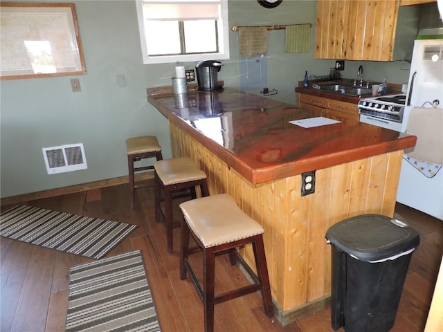 kitchen with a peninsula, a sink, visible vents, range with gas stovetop, and wood finished floors