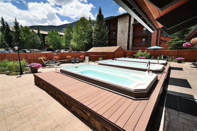 view of pool featuring a patio area, a fenced backyard, hot tub deck surround, and a mountain view