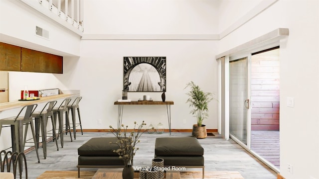 living area with light wood-style floors, visible vents, a towering ceiling, and baseboards