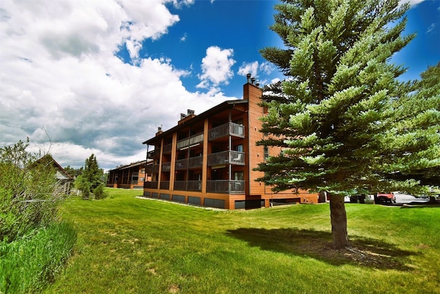 back of house with a lawn, a chimney, and a balcony
