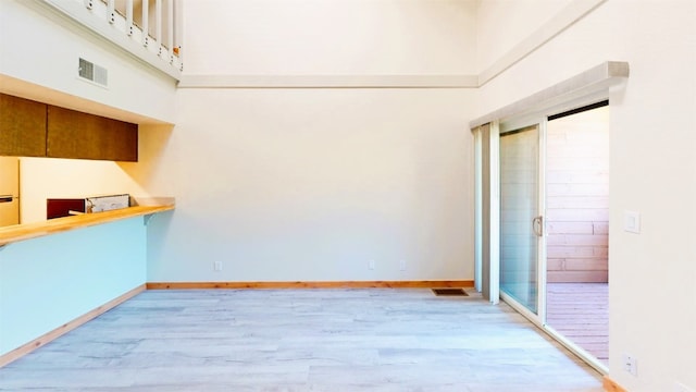 unfurnished room featuring visible vents, a towering ceiling, light wood-style flooring, and baseboards