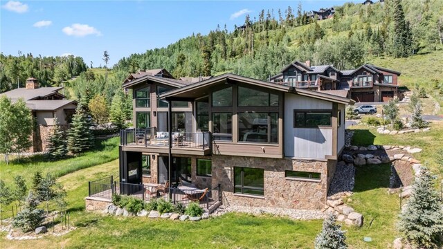 304 Raven Golf Ln, Silverthorne, CO 80498 - back of property featuring stone siding, a forest view, a wooden deck, a lawn, and a patio