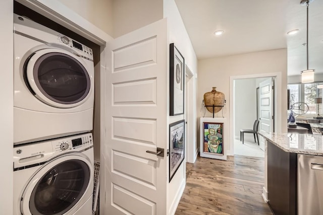 clothes washing area with stacked washer / drying machine, wood finished floors, laundry area, and recessed lighting