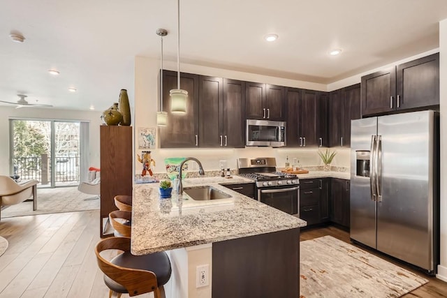kitchen with a kitchen breakfast bar, stainless steel appliances, a sink, light stone countertops, and a peninsula