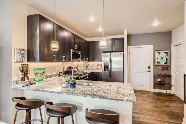 kitchen featuring a peninsula, dark brown cabinetry, stainless steel appliances, and a breakfast bar area