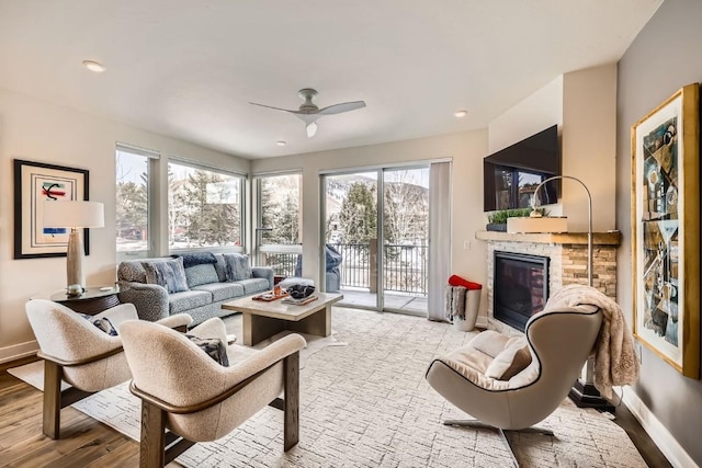 living area with wood finished floors, a ceiling fan, baseboards, and a fireplace