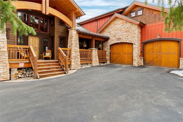 view of front of house with a porch, an attached garage, driveway, and stone siding