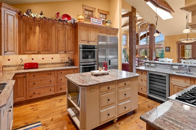kitchen with appliances with stainless steel finishes, light stone counters, a sink, wine cooler, and a skylight