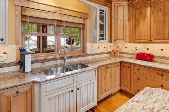 kitchen featuring a sink, glass insert cabinets, light stone countertops, and tasteful backsplash