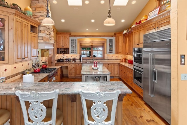 kitchen featuring tasteful backsplash, light stone counters, light wood finished floors, a skylight, and stainless steel appliances