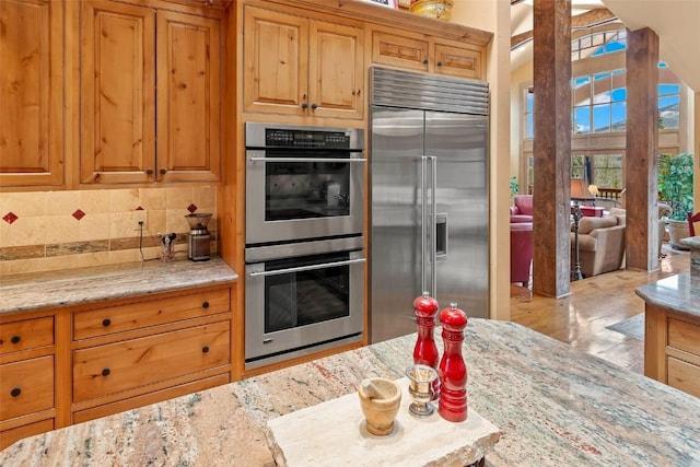 kitchen with backsplash, brown cabinets, light stone countertops, and appliances with stainless steel finishes