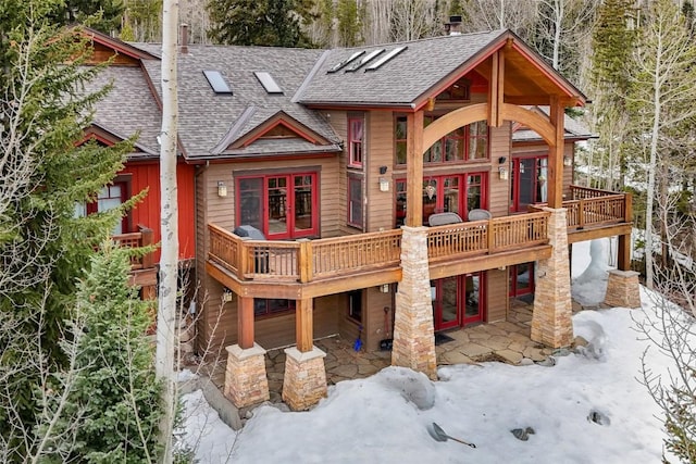 snow covered property featuring french doors, a patio, a shingled roof, and a deck