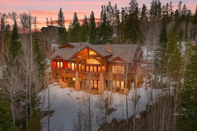 back of house at dusk with a chimney, a shingled roof, and a wooden deck
