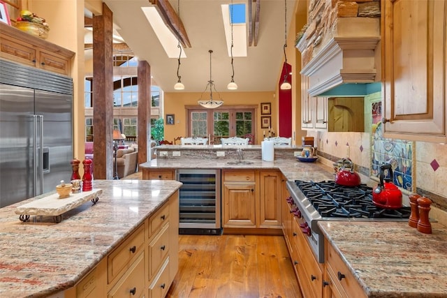 kitchen featuring a peninsula, custom exhaust hood, beverage cooler, light wood finished floors, and appliances with stainless steel finishes