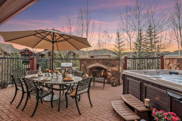 view of patio featuring a hot tub, an outdoor stone fireplace, and outdoor dining space