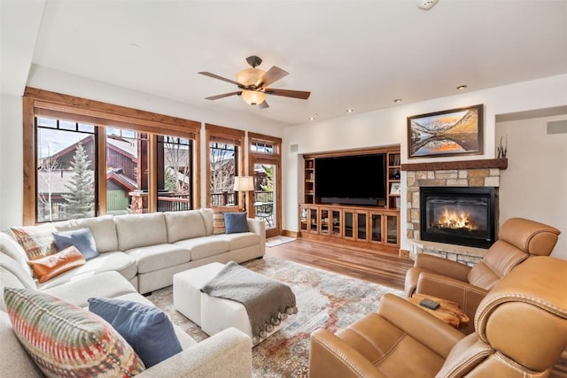 living area with plenty of natural light, a ceiling fan, wood finished floors, and a stone fireplace
