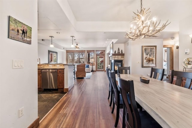 dining area featuring dark wood finished floors, ceiling fan with notable chandelier, and a fireplace