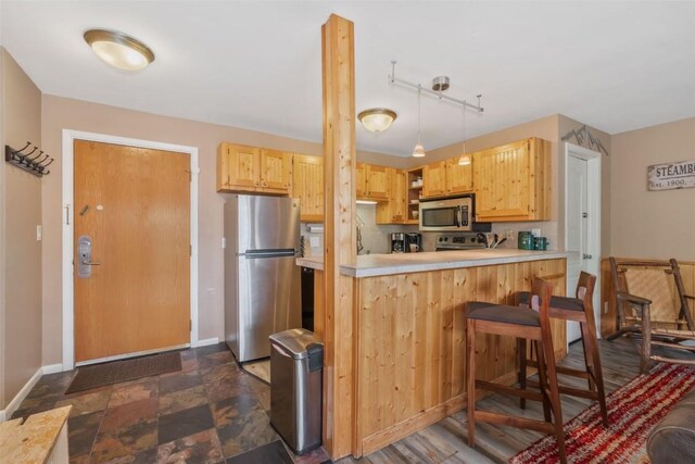 kitchen with appliances with stainless steel finishes, baseboards, light countertops, a breakfast bar area, and a peninsula