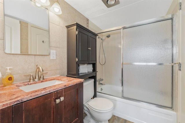 bathroom with tile walls, backsplash, shower / bath combination with glass door, vanity, and toilet