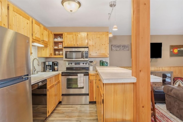 kitchen featuring appliances with stainless steel finishes, a sink, light countertops, light brown cabinets, and light wood finished floors
