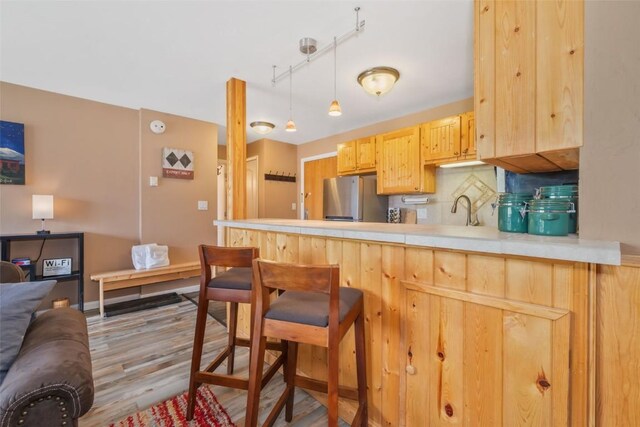 kitchen with freestanding refrigerator, a peninsula, tasteful backsplash, a kitchen bar, and wood finished floors