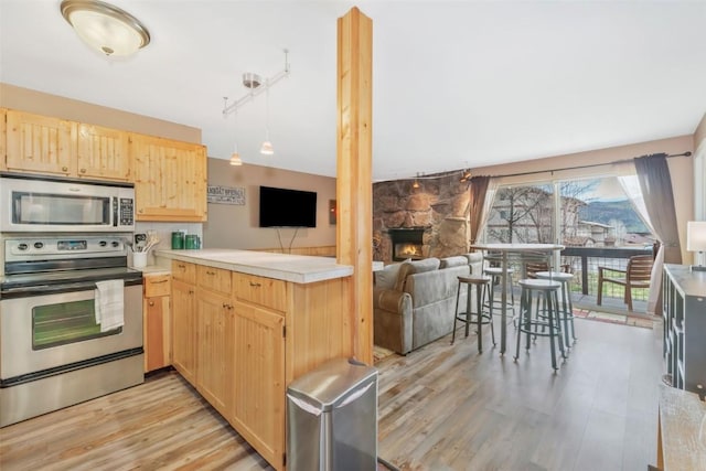kitchen with stainless steel appliances, light brown cabinets, open floor plan, light wood-style floors, and a peninsula
