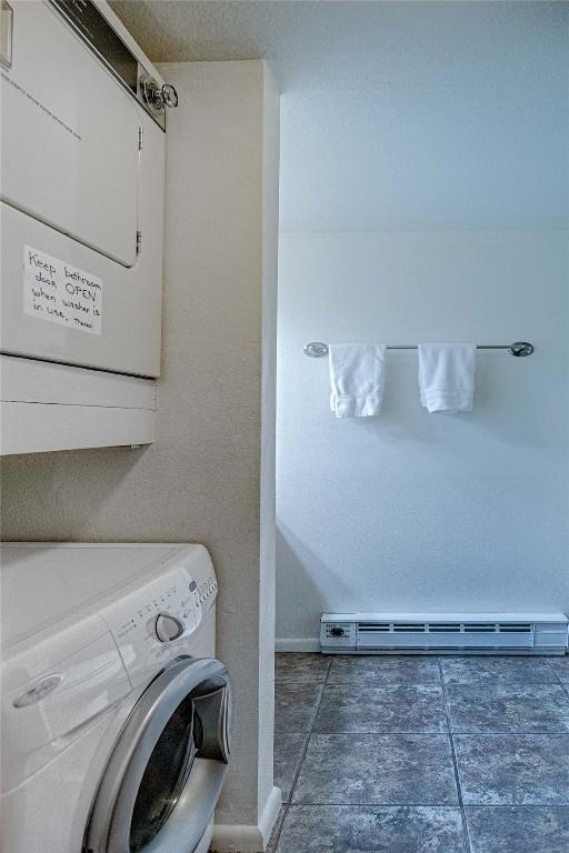 clothes washing area featuring a baseboard heating unit, stacked washer and clothes dryer, and laundry area