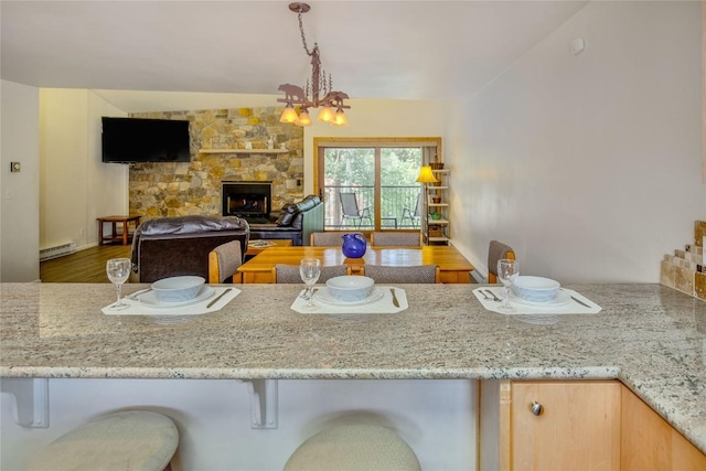 kitchen featuring light stone counters, a stone fireplace, wood finished floors, a baseboard radiator, and a notable chandelier