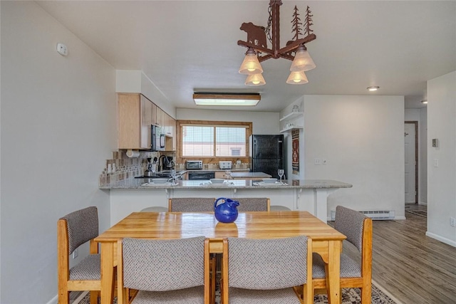 dining room with a baseboard heating unit, light wood finished floors, and baseboards