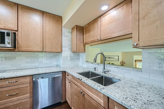 kitchen with a sink, stainless steel appliances, decorative backsplash, and light stone counters