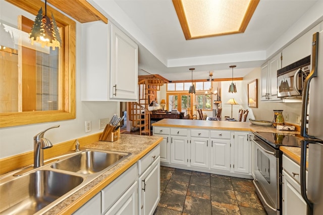 kitchen with white cabinets, stainless steel appliances, a sink, stone finish flooring, and a peninsula