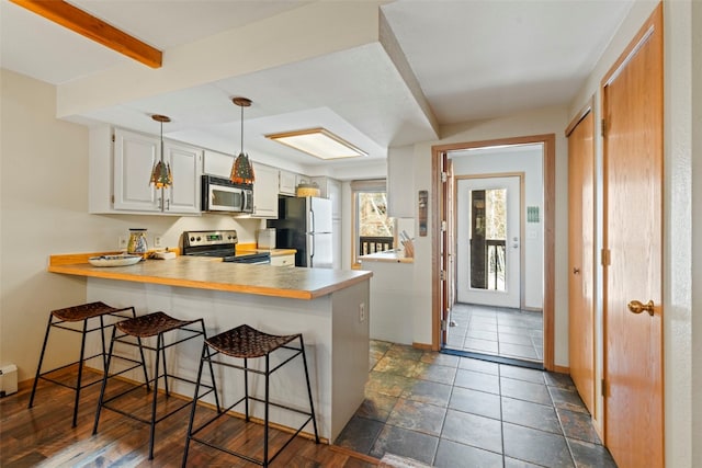 kitchen with stainless steel appliances, a peninsula, baseboards, a kitchen bar, and white cabinetry