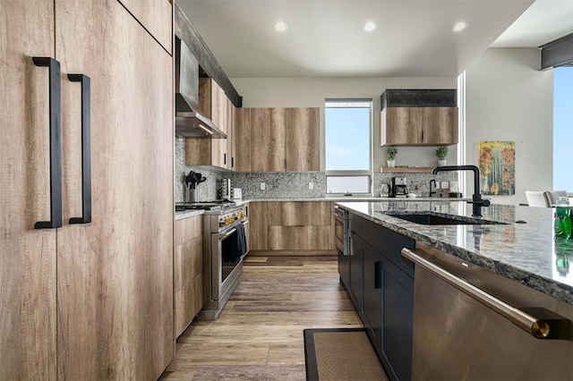 kitchen with a sink, light wood-style floors, dark stone counters, stainless steel appliances, and recessed lighting