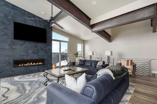 living area featuring ceiling fan, a fireplace, baseboards, vaulted ceiling with beams, and wood finished floors