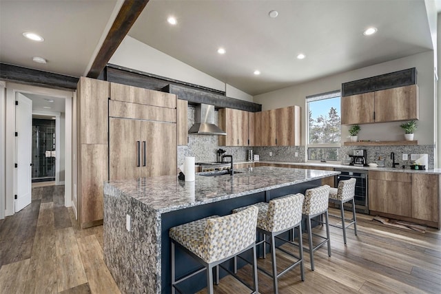 kitchen featuring wall chimney range hood, light stone counters, backsplash, and beverage cooler