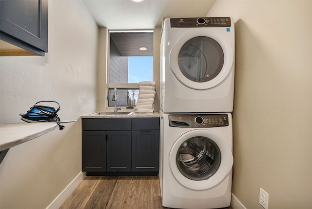laundry area featuring cabinet space, wood finished floors, a sink, baseboards, and stacked washer and clothes dryer