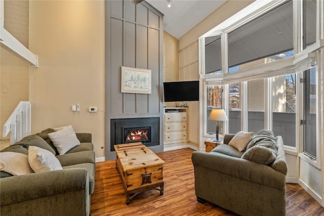 living area featuring a glass covered fireplace, baseboards, wood finished floors, and high vaulted ceiling