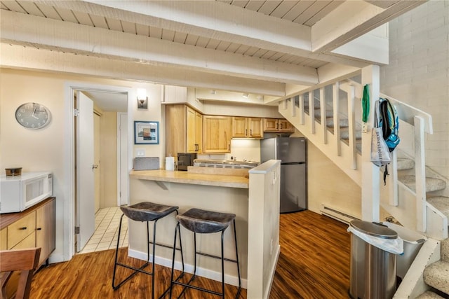 kitchen with a breakfast bar area, freestanding refrigerator, white microwave, baseboard heating, and dark wood-style flooring