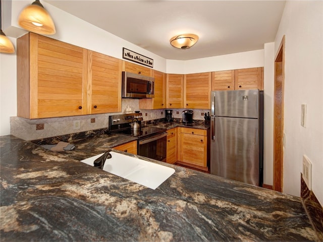 kitchen featuring a sink, dark stone countertops, appliances with stainless steel finishes, and tasteful backsplash