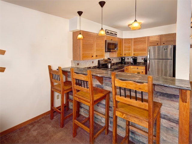 kitchen featuring dark countertops, hanging light fixtures, baseboards, appliances with stainless steel finishes, and carpet flooring
