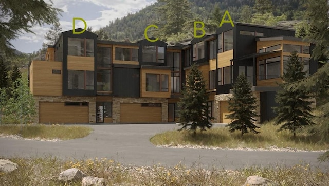 view of building exterior featuring an attached garage, a wooded view, concrete driveway, and a mountain view