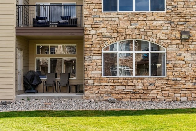 exterior space with stone siding, a balcony, and a patio