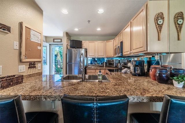 kitchen featuring stainless steel appliances, a kitchen breakfast bar, light brown cabinetry, a sink, and a peninsula