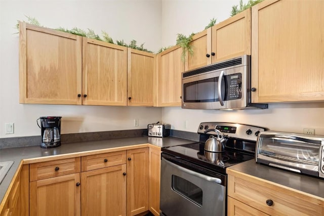 kitchen with a toaster, dark countertops, light brown cabinetry, and stainless steel appliances